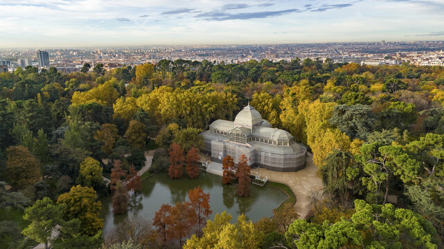 Aerial view of Parque el Retiro with the beautiful Palacio de Cristal surrounded by vibrant autumn foliage and a serene pond, Retiro, Madrid, Spain.