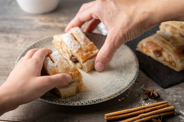 hands taking two pieces of apple strudel on a wooden table
