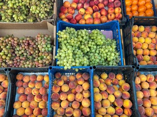 Assorted fresh fruits including peaches, grapes, and persimmons, colorful and ripe, arranged together in crates or baskets, ready for sale or display.