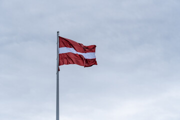 Latvian National Flag Waving on Tall Flagpole Against Overcast Sky – Symbol of Freedom and Unity