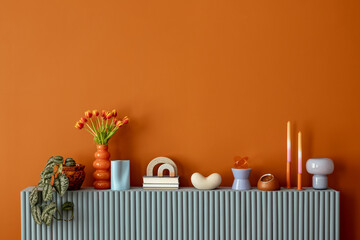Minimalist orange wall with sideboard decorated with tulips, candles and contemporary decorative objects. Copy space.