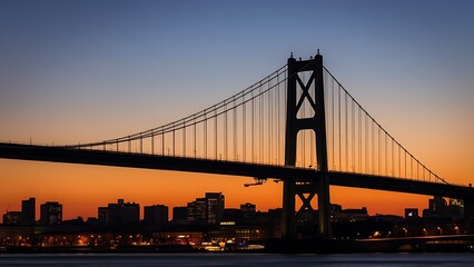 Fototapeta premium Silhouetted suspension bridge at dusk with city lights