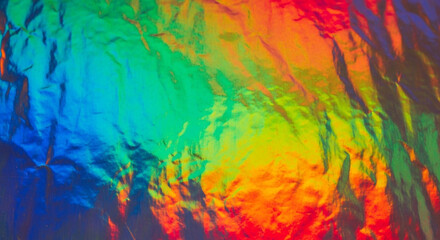 Colorful abstract texture of a crumpled holographic foil showing a vibrant spectrum of rainbow light and gradients.