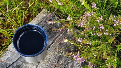 Stainless steel cup with herbal organic tea placed on a weathered wooden surface surrounded by wild...
