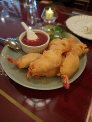 Fried shrimp tempura with dipping sauce served on a plate in a restaurant setting