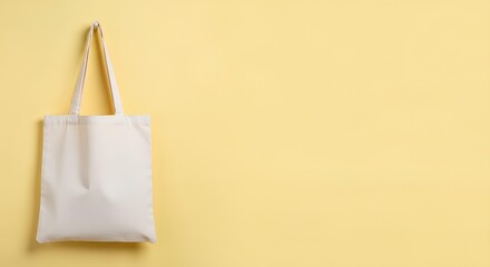 Blank white canvas tote bag hanging on a yellow wall. Eco friendly shopping bag mockup with copy space for branding or design.