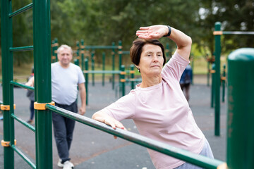 Obraz premium elderly woman doing exercises on a horizontal bar at an outdoor sports ground