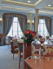 Formal and elegant ocean view dining room restaurant onboard luxury cruiseship or cruise ship liner with set tables in Art Deco interior design style and ceiling ambient lighting