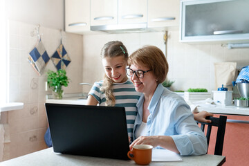 Happy woman and teenager using laptop at home kitchen. Working mother and daughter have fun together. Technology lifestyle, distance education, learning. Video call, receiving school acceptance email