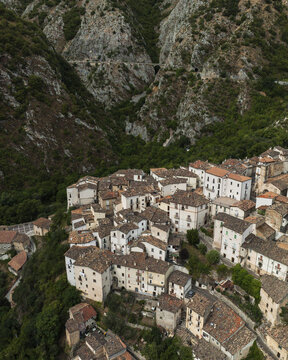 Aerial view of a charming Italian village nestled amongst verdant trees, with white buildings contrasting against the rugged, rocky mountainside, Anversa degli Abruzzi, Abruzzo, Italy.
