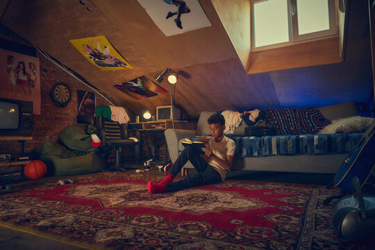 Teen boy reading notebook in retro attic bedroom. Concept of education, creativity, personal space, and emotional growth with nostalgic 90s room decor.
