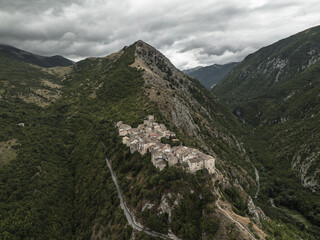 Aerial view of an ancient village clinging to a precipitous ridge, embraced by verdant slopes under a brooding sky, Castrovalva, Abruzzo, Italy.