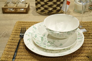 Elegant ceramic dinnerware set featuring a floral design, neatly arranged on a woven placemat. Includes a bowl, plate, and cutlery, perfect for a sophisticated dining setting