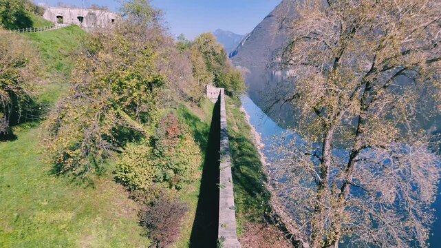 lake Idro next to a grassy slope, with a stone wall and Rocca d'Anfo in the distance