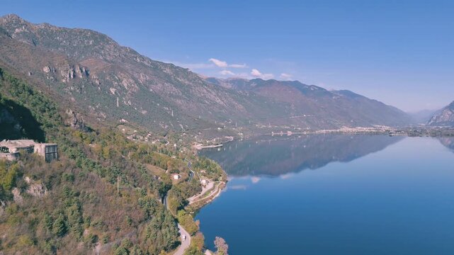 lake Idro reflecting a mountainous shoreline, with a road and Rocca d'Anfo nestled on it in Italy
