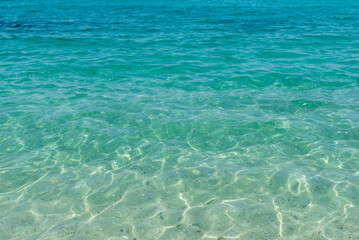 Shallow turquoise sea with sunlight reflections creating mesmerizing patterns on sandy bottom, perfect for summer and tropical themes