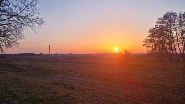 Sonnenuntergang  im Blockland Bremen - Wiese eingerahmt von zwei B&auml;umen mit tiefgelber Sonne, ,Himmel von rot &uuml;ber orange und rosa bis blau. mit Fallturm und Fernsehturm am Horizont.