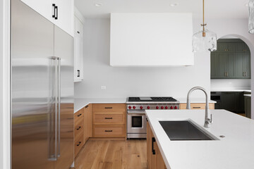 A kitchen with white and natural white oak cabinets, pendant lights hanging over a large island,...