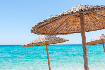 Straw beach umbrellas by turquoise sea on a sunny day, symbolizing summer relaxation and coastal vacations