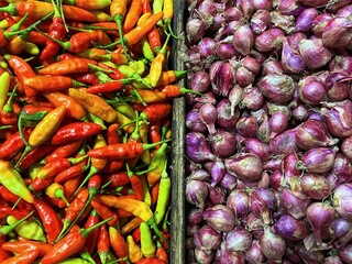 A close-up view of fresh red chili peppers on the right and red shallots on the left, arranged side by side, showcasing vibrant color and natural texture.