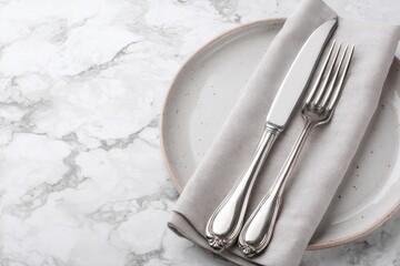 Elegant place setting  Grey linen napkin, silver cutlery on a speckled off-white plate atop a marble surface