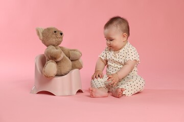 Cute little baby sitting near potty with toy bear on pink background