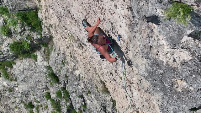 AERIAL: Agile young woman quickly climbs a steep rock face. Her focus and body position illustrate the skill and physical demands of the climb. Challenging adrenaline sport activity for summer days.