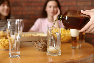 Woman pouring beer into glass at wooden table indoors, selective focus