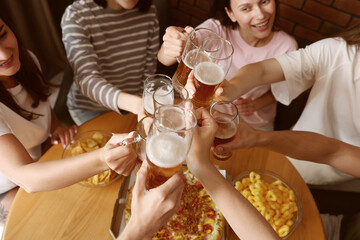 Group of happy friends clinking glasses of beer at table indoors, above view
