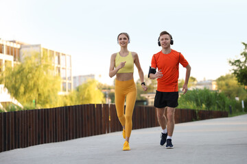 Obraz premium Happy couple in headphones running outdoors, low angle view. Morning exercise
