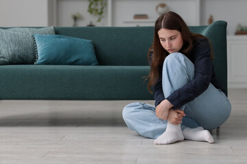 Obraz premium Sad young woman sitting on floor at home, space for text