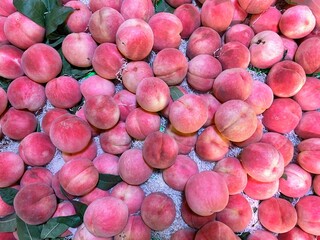 Fresh pink peaches piled in bulk at a market stall, top view. Vibrant ripe fruit with natural texture and green leaves, perfect for food, freshness, and healthy lifestyle themes.