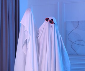 Funny ghost. Man covered with white sheet in blue light at home