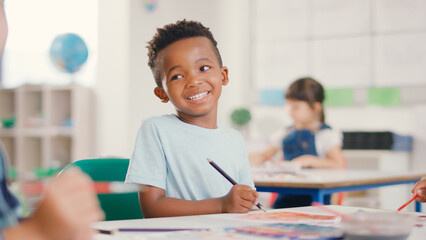 Portrait Of Smiling Male Elementary School Student Sitting At Table Painting