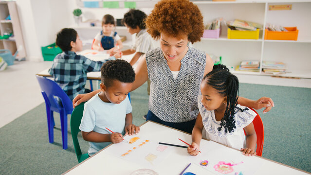 Female Elementary School Teacher Sitting With Students Around Table Painting