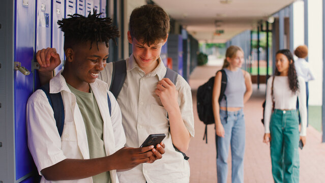 Two Male High School Or Secondary Students Looking At Social Media Or Internet On Phone By Lockers