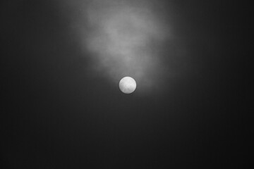 Full moon or sun obscured by clouds in dark night sky, minimalistic black and white atmospheric photography with mysterious mood