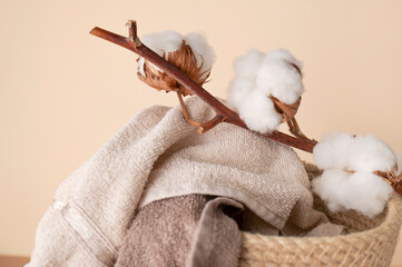 Natural wicker basket with cotton towels, branch and cotton flowers on beige background....