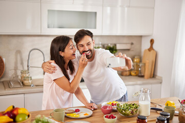 In a sunny kitchen, a couple smiles and playfully takes a selfie together while preparing a meal. Fresh ingredients and joy fill the atmosphere as they bond over cooking.