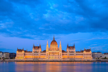 Fototapeta premium The majestic Parliament Building in Budapest illuminates the twilight sky, reflecting in the Danube River. This architectural wonder is a symbol of Hungary's rich history and culture.