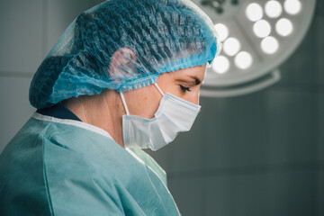 Female surgeon in green scrubs and surgical mask, focused on patient care in operating room, illuminated by bright surgical lights, showcasing dedication to medical profession and teamwork