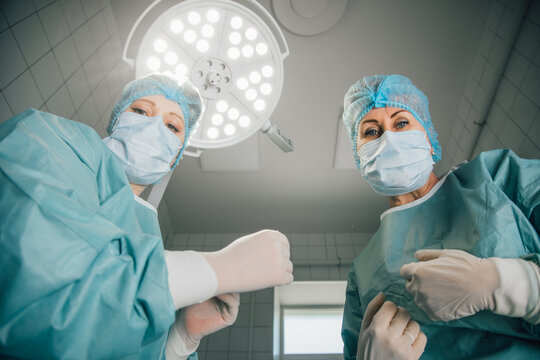 Two female surgeons in surgical scrubs and masks, preparing for an operation under bright surgical lights, showcasing teamwork and professionalism in a modern operating room environment