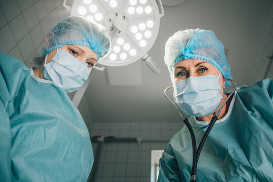 Two female surgeons in surgical scrubs and masks, preparing for an operation under bright surgical lights, showcasing teamwork and professionalism in a modern operating room environment