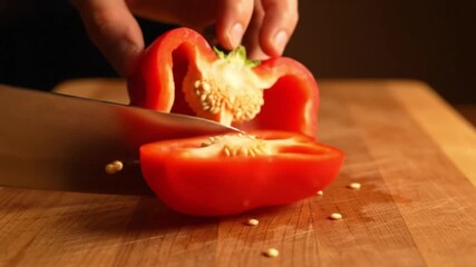 A person uses a knife to slice a red bell pepper in half on a wooden cutting board. - Powered by Adobe