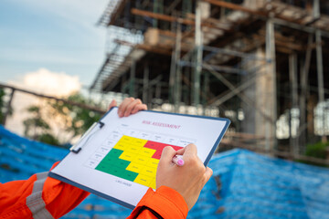 Action of a project manager is writing on risk assessment matrix form to rating the risk of house building structure or building quality (as blurred background. Industrial working scene, close-up.