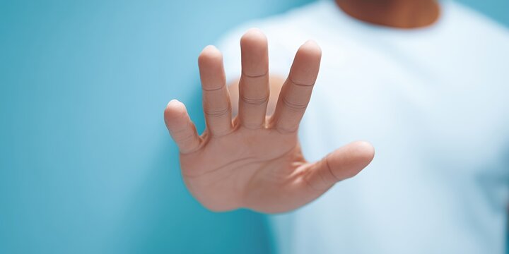 Close-up of a hand raised in a stop gesture against a soft blue background, conveying a message of pause or caution in a calm and serene atmosphere
