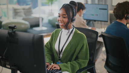 Cheerful customer service representative wearing headset is working her desk modern office environment. She is engaging with client while typing her keyboard, showcasing professionalism
