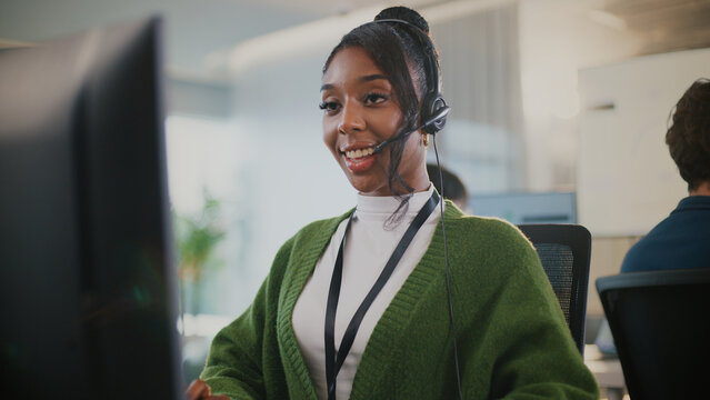 Confident African American female call center agent communicates with clients using headset and computer. She offers professional tech support at a modern office desk, smiling diverse office - Powered by Adobe