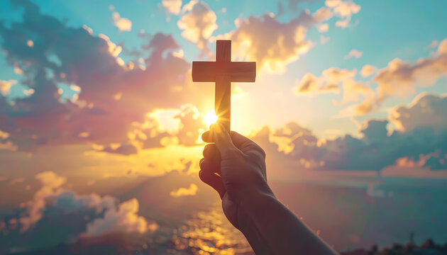 Hand holding cross silhouetted against sunset sky with warm colors