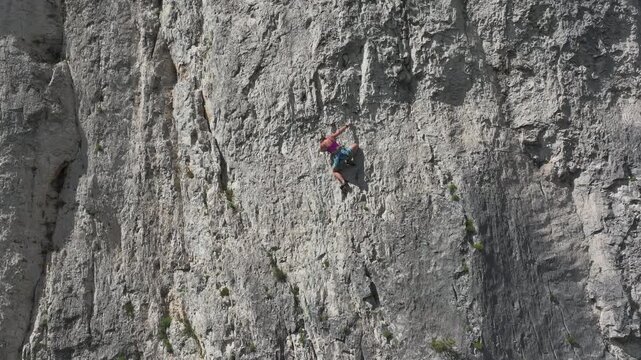 AERIAL: Woman climbs a steep and challenging route in natural rock climbing area. Scenic and vast vertical wall offers endless possibilities for adrenaline sports enthusiasts in a natural setting.